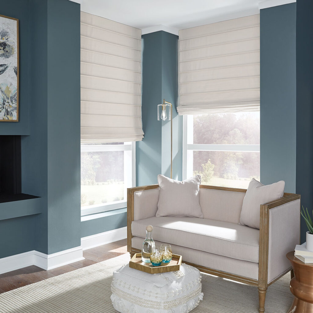 A medium blue living room with light neutral furniture and off-white Front Fold Roman Shades on the windows.