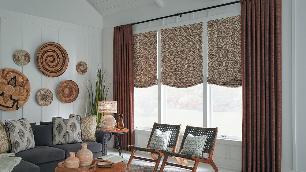 A casual living room in warm reds and browns featuring Carole Fabrics Rod Pocket Drapery on Forest Deapery Hardware with french Returns and Soft Roman Shades.