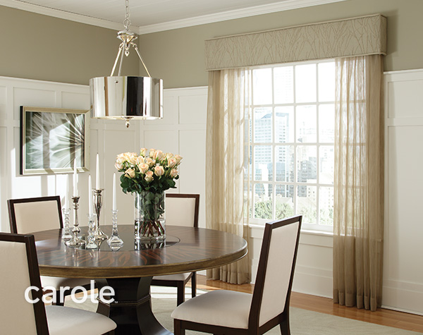 A dining room in soft beige and gold with sheer side panels and a cornice on the window.