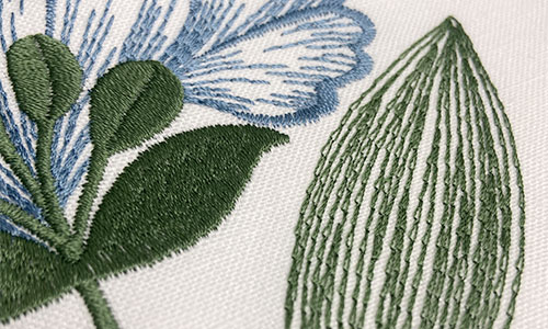 Detail of a green embroidered leaf next to a blue embroidered flower on a white background fabric.