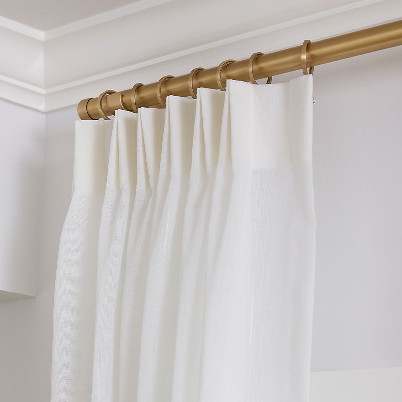 White custom pleated drapery on golden drapery hardware.