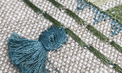 Detail of fringe stitch embroidery next to rows of embroidered stitches on a light beige background.