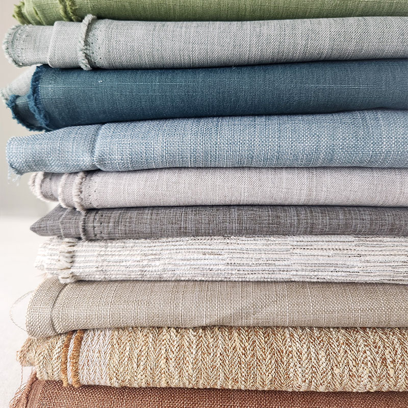 A stack of folded solid ad textured fabrics in a wide range of colors from the Everyday Basics Collection by Carole Fabrics.