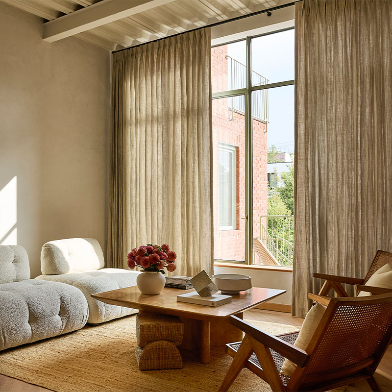A neutral living room with beige drapery on PowerView Motorized Drapery Hardware over a wall of windows.