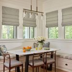 A kitchen dining nook featuring four Front Fold Romans Shades on thw windows over padded bench seating.